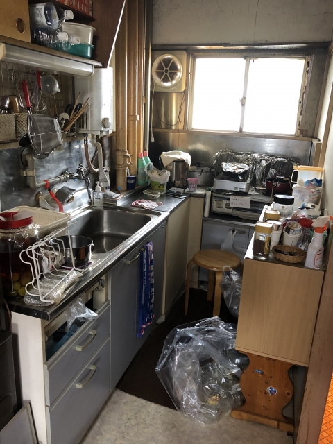 Cramped kitchen area with double sink, dish rack, cluttered countertops, and a window above the counter.